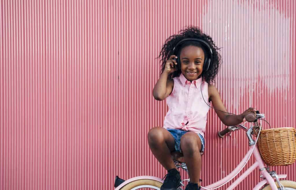 Bambina felice che ascolta musica e sorride con la bicicletta. Infanzia all'aperto